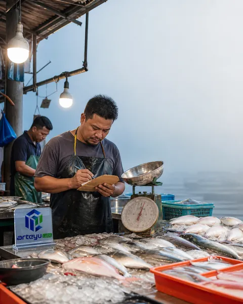 Gerai ikan pasar basah waktu subuh, penjual menulis di buku nota, tanda logo di tiang